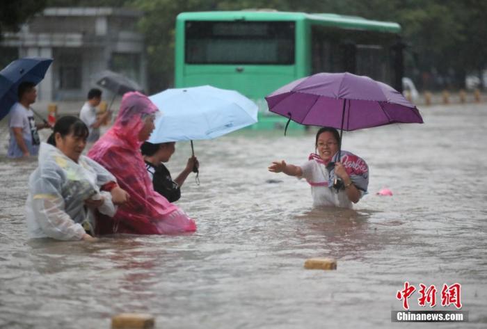7月20日，郑州遭遇强降雨，在经三路、农业路上，市民互相帮助走在齐腰深的积水里。 图片来源：视觉中国